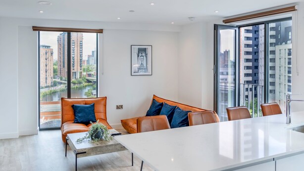Una sala de estar moderna con sofá, mesa de centro y ventana grande con vista a edificios altos y un río.