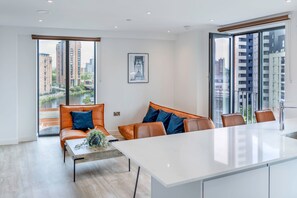Un salon moderne avec un canapé, une table basse et une grande fenêtre donnant sur des immeubles imposants et une rivière.