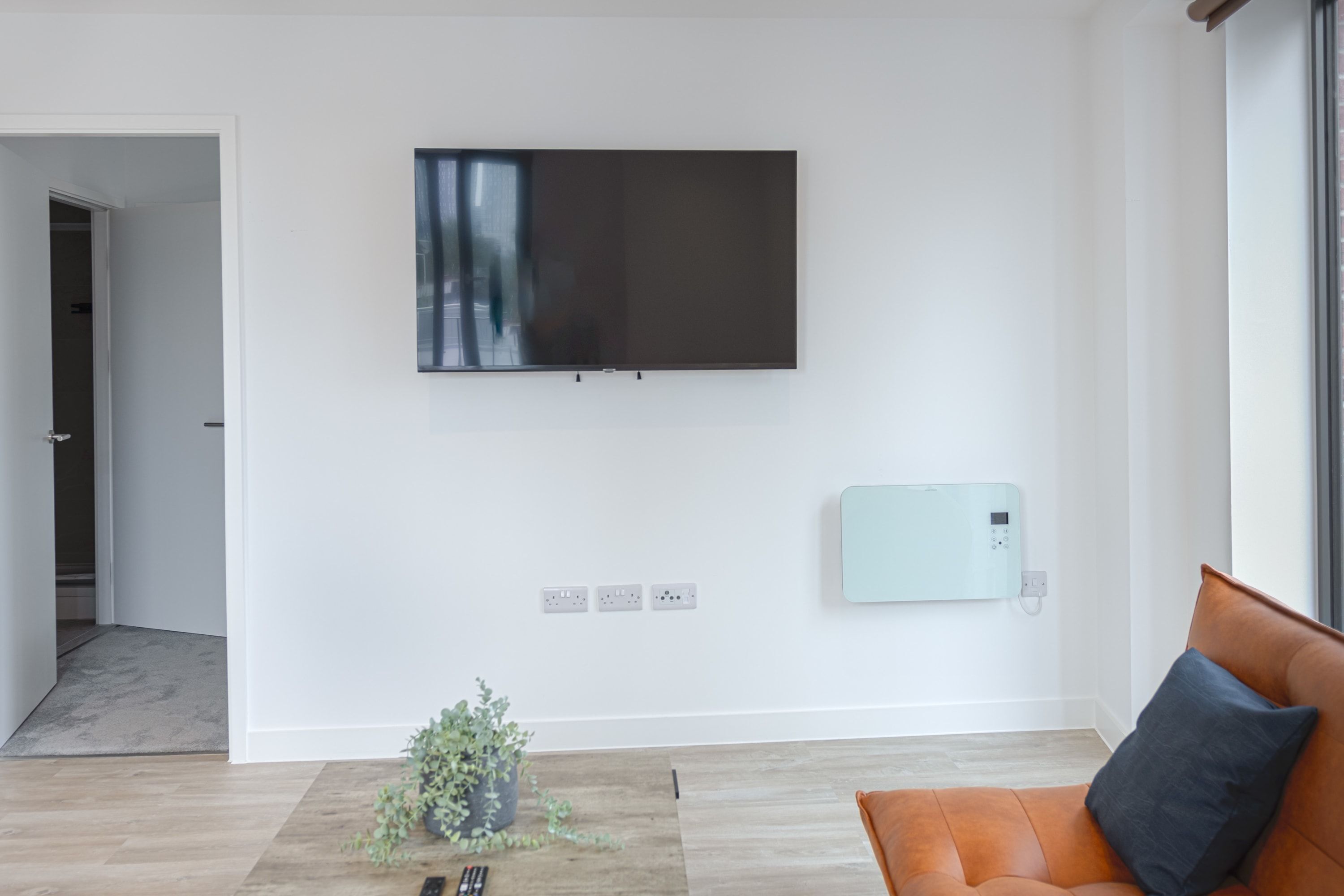 Uma sala de estar moderna com televisão de tela plana na parede, uma poltrona de massagem e um pequeno vaso com planta no chão.
