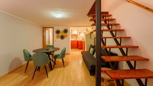 Um interior moderno com uma escada de madeira, uma sala de jantar com mesa e cadeiras redondas, e uma cozinha ao fundo.