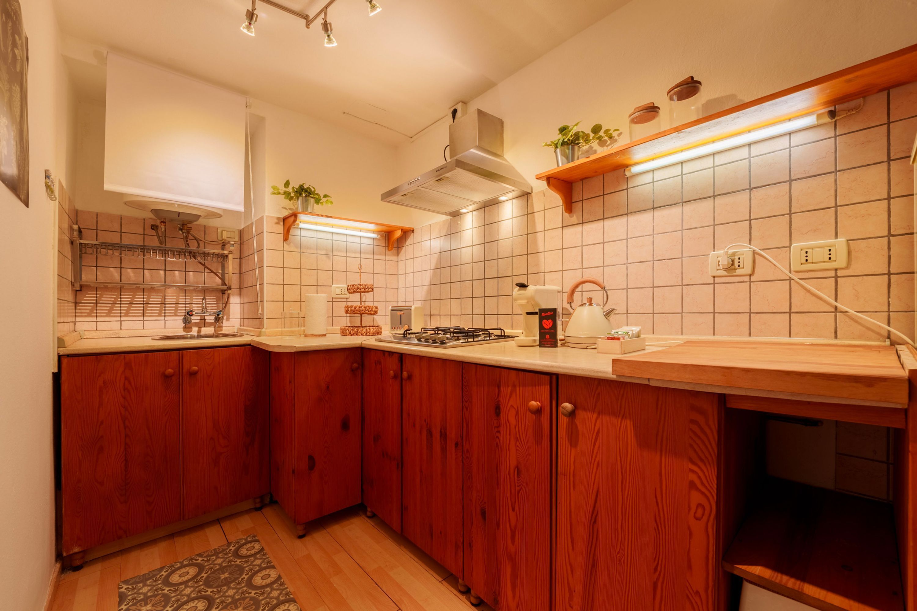 Una cocina con armarios de madera, estufa a gas, pileta y campana extractora.