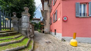 A cobblestone street with a red building, a yellow bollard, and a speed limit sign. - Beach Lake Bellagio by Wonderful Italy (Bellagio)