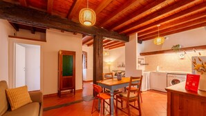 A cozy room with a wooden ceiling, a dining table with chairs, a sofa, and a kitchen area with a washing machine. - Beach Lake Bellagio by Wonderful Italy (Bellagio)