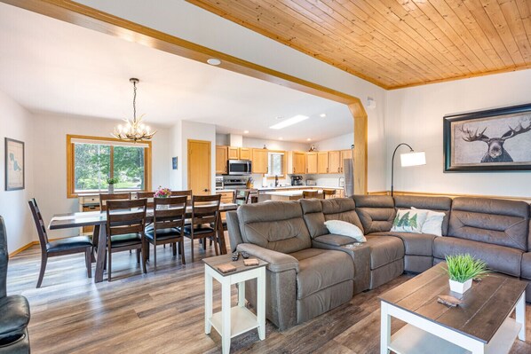 A spacious living room with a large sectional sofa, a dining area with wooden chairs, and a kitchen with wooden cabinets.