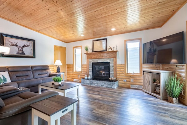 Una sala de estar acogedora con chimenea, techo de madera y un televisor grande.