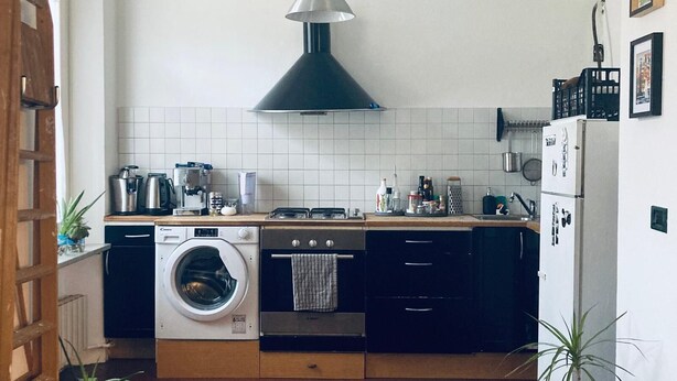 A compact kitchen with a washing machine, oven, and a hanging light fixture.
