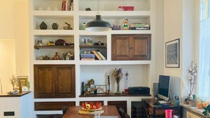 A dining area with a wooden table and chairs, surrounded by shelves with books and decorative items.