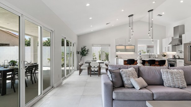 A spacious living area with a grey sofa, a dining table, and a kitchen in the background.
