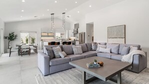 A modern living room with a grey sectional sofa, a coffee table, and a dining area with a white table and chairs.