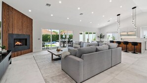 A modern living room with a fireplace, grey sofa, and a kitchen area with bar stools.