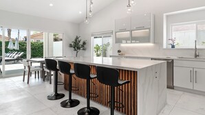 A modern kitchen with a central island, bar stools, and a view of the outdoors.