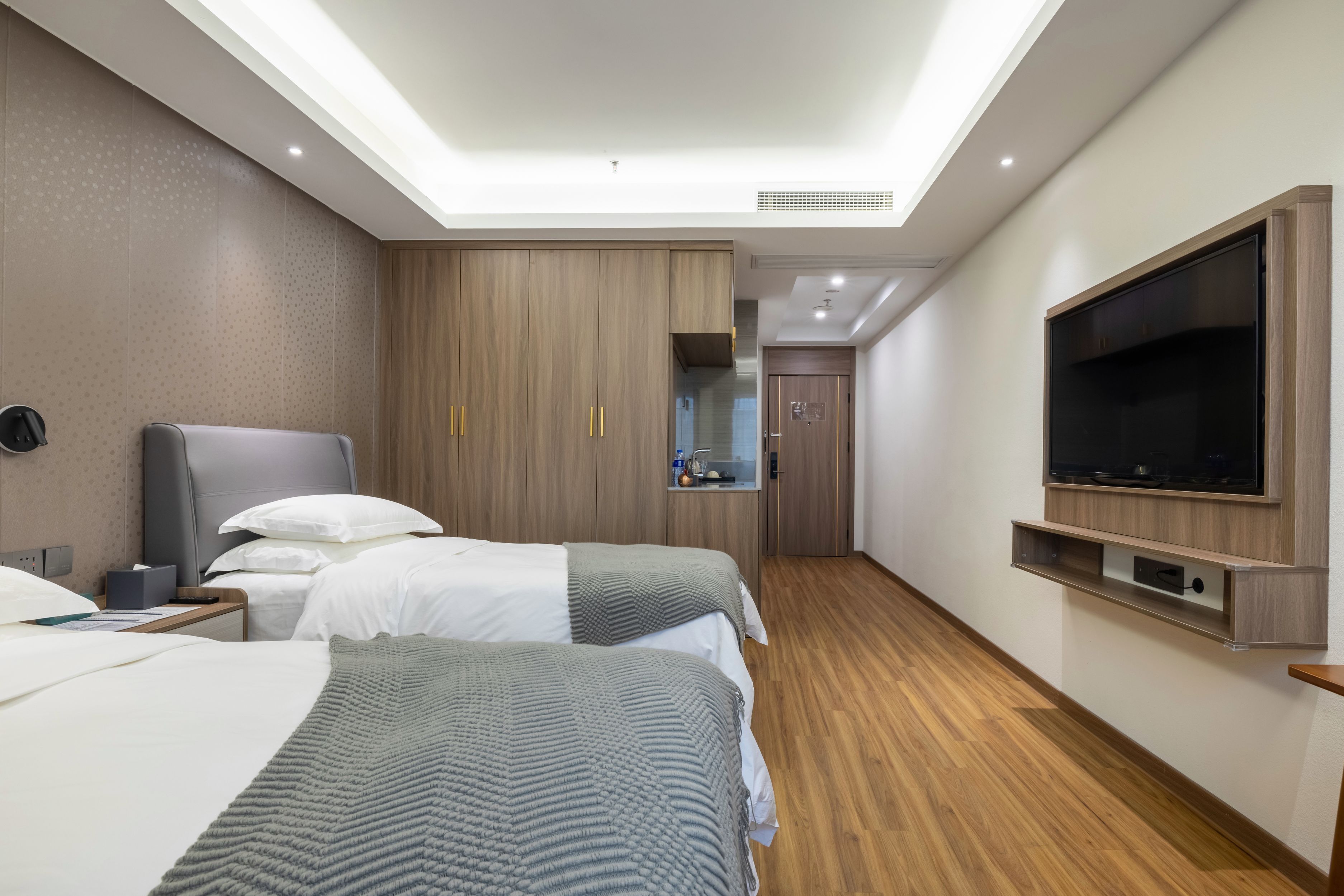 A hotel room with two beds, a TV, a desk, and a bathroom visible through a glass door.
