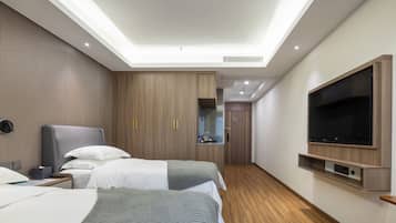 A hotel room with two beds, a TV, a desk, and a bathroom visible through a glass door.