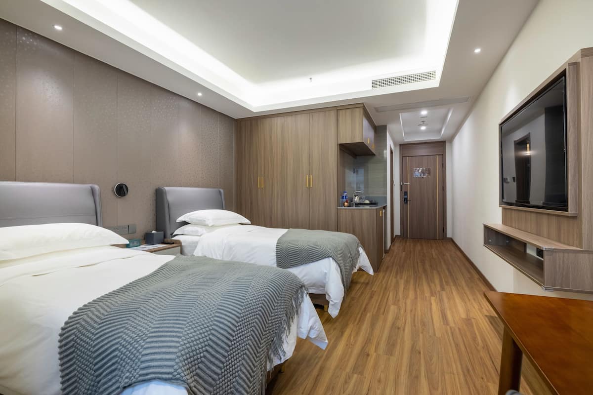 A hotel room with two beds, a TV, a desk, and a bathroom.
