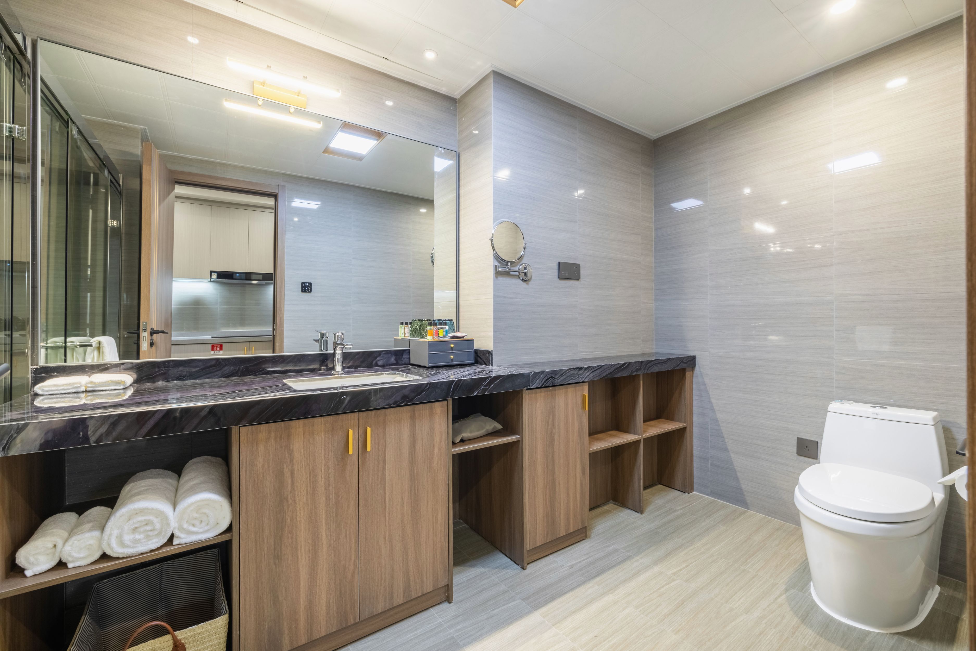Ein modernes Badezimmer mit Marmorplatte, Holzschränken, einem großen Spiegel und einer Toilette.