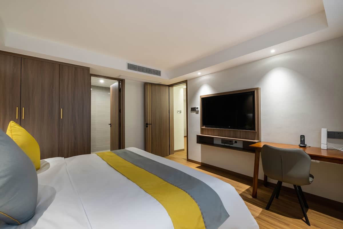 A hotel room with a bed, a desk, a chair, a television, and a wardrobe.