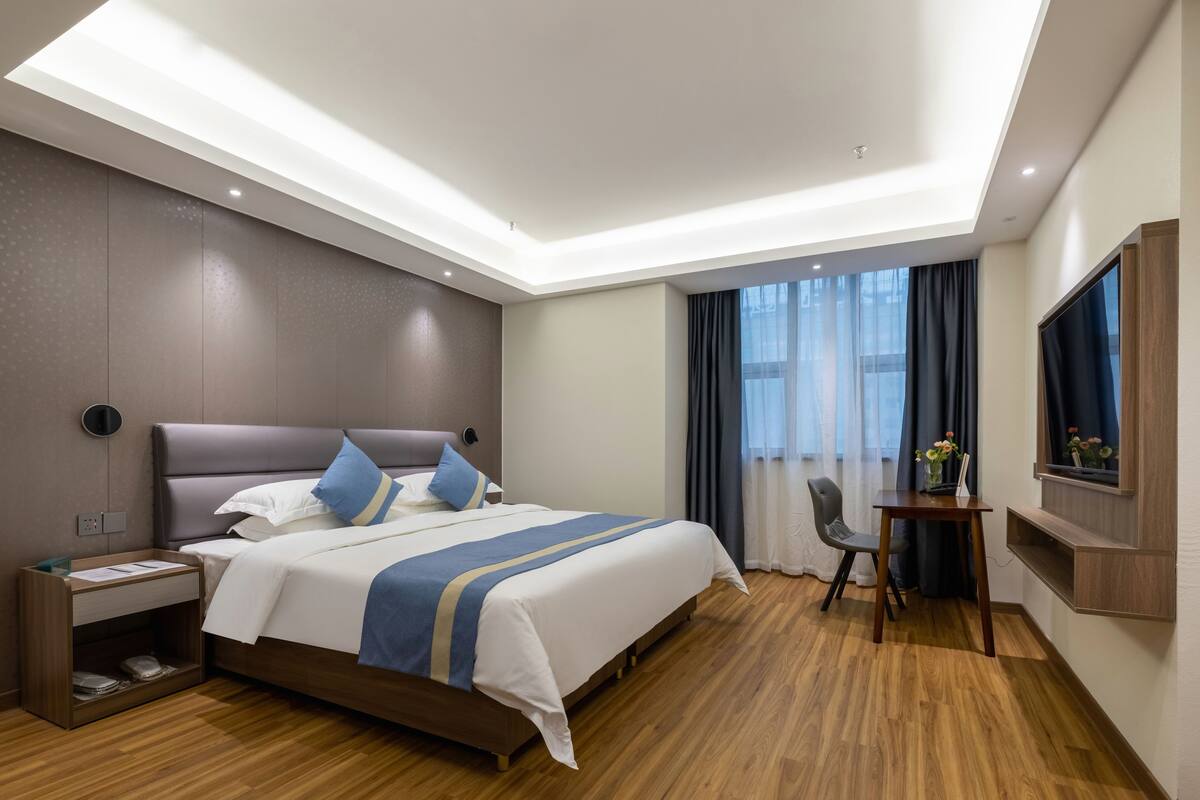 A modern hotel room with a large bed, bedside table, and a TV mounted on the wall.