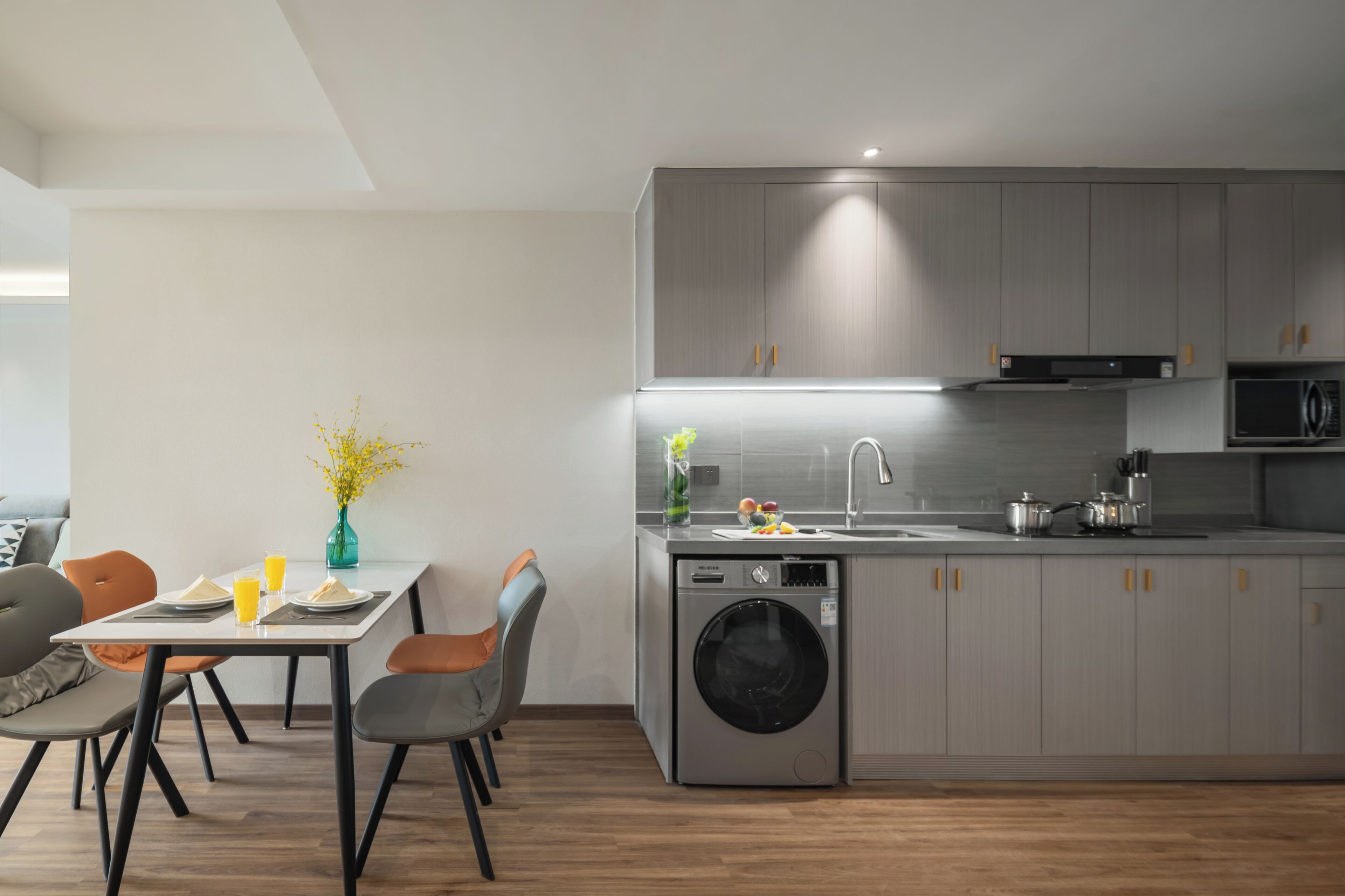 A modern kitchen with grey cabinets, a built-in washing machine, and a dining area with a table and chairs.