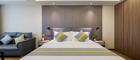 A modern hotel room with a large bed, a sofa, and a wooden wardrobe.
