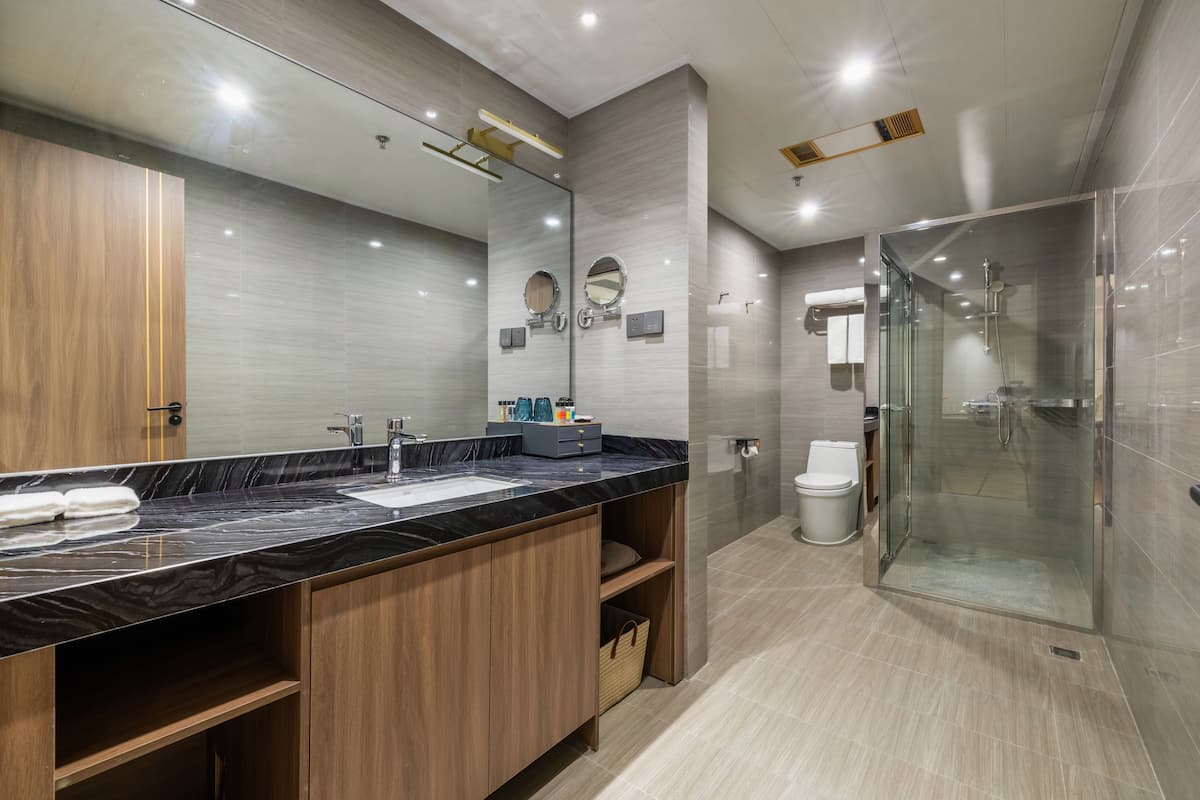 A modern bathroom with a marble countertop, wooden cabinets, a large mirror, and a glass-enclosed shower.