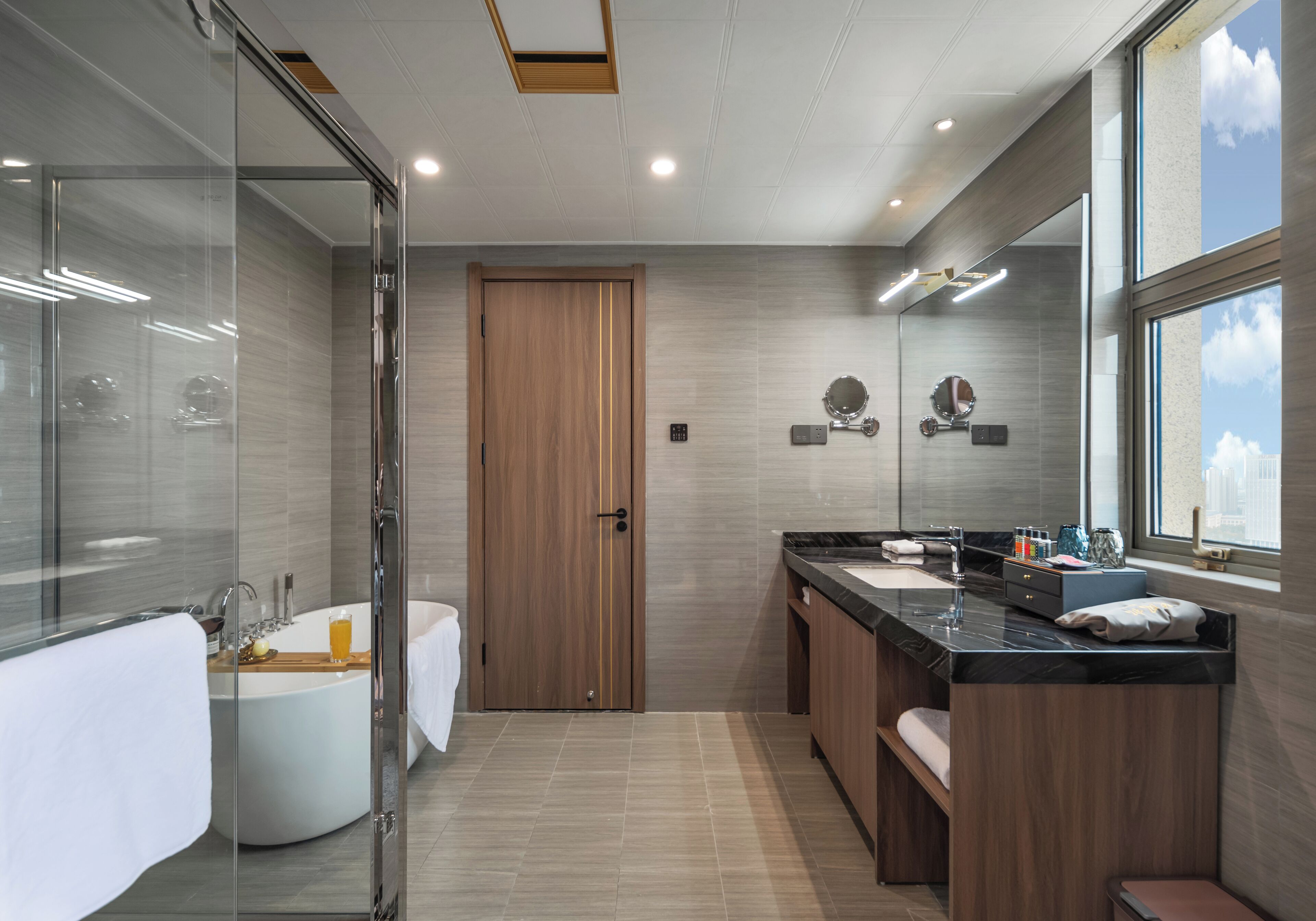 A modern bathroom with a glass shower enclosure, a freestanding bathtub, a vanity with a black countertop, and a large mirror.