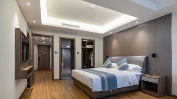 Ein modernes Hotelzimmer mit einem großen Bett, einem Nachttisch, einem integrierten Fernseher und einem begehbaren Kleiderschrank.