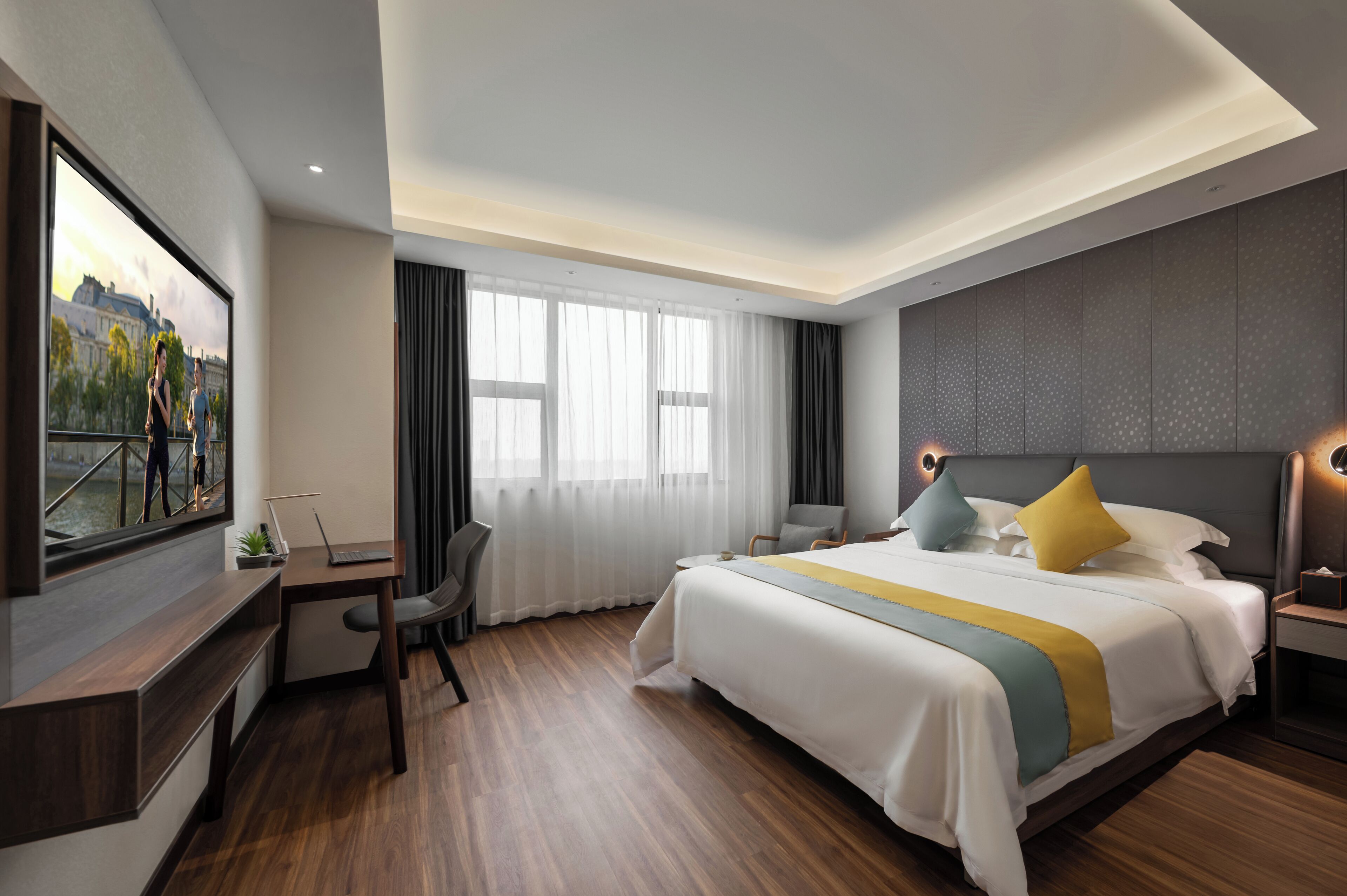 A modern hotel room with a large bed, a desk, and a chair. There is a large window with curtains, a flat-screen TV mounted on the wall, and a nightstand with a lamp.