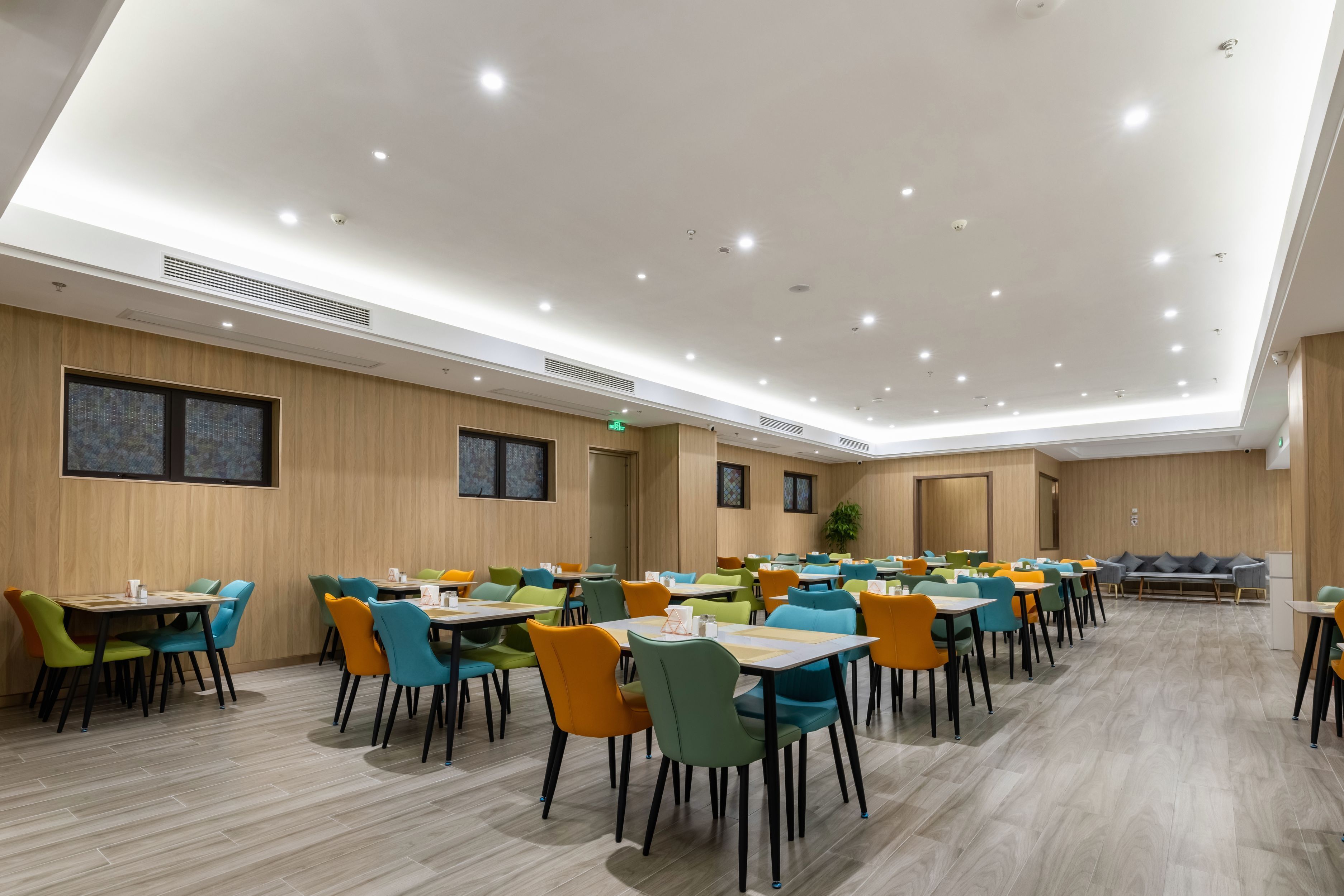 Un vaste espace dédié à la salle à manger, avec de nombreuses tables et chaises, des murs en bois et des spots encastrés au plafond.