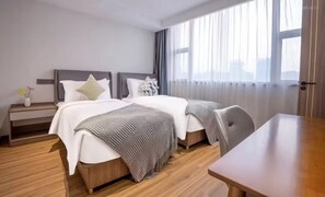 Una habitación de hotel moderna con dos camas, suelo de madera, un escritorio y un amplio ventanal con cortinas translúcidas.
