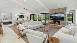A modern living room with a fireplace, white sofas, and a large TV.