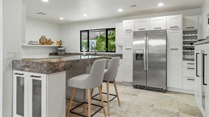 A modern kitchen with white cabinets, a stainless steel refrigerator, and a granite countertop.