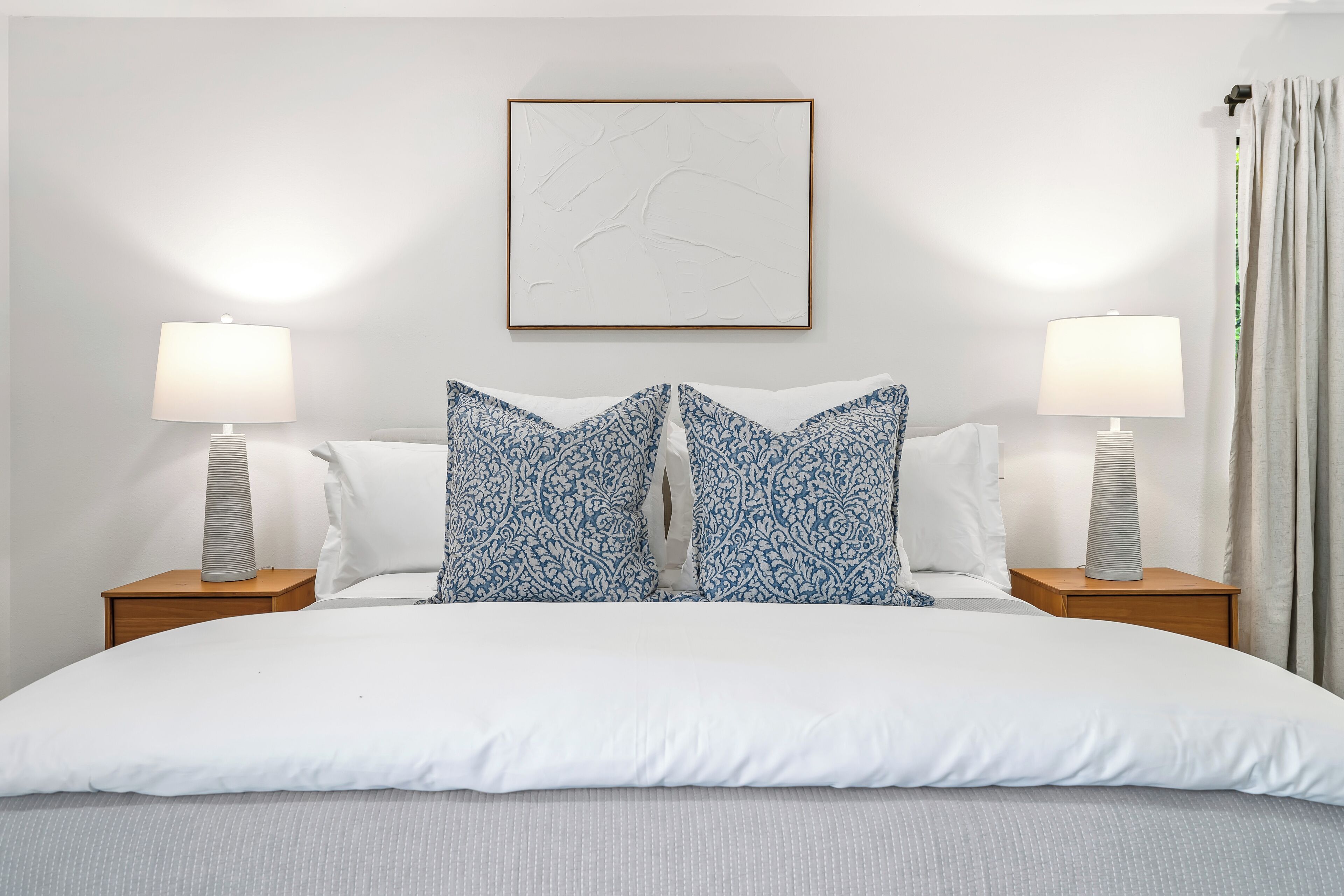 A neatly arranged bedroom with a large bed, two bedside tables with lamps, and a framed artwork on the wall.