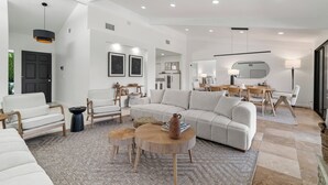 A spacious living room with a large sofa, two armchairs, a coffee table, and a dining area with a table and chairs.