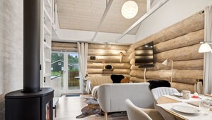 Een gezellig kamer in blokhutstijl, met een houtkachel, een bank, een eettafel met bord en beker, en een aan de muur bevestigde televisie.