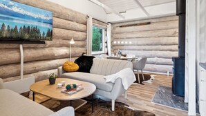 Een knus blokhutinterieur met een houten wand, een bank, een salontafel en een eethoek.
