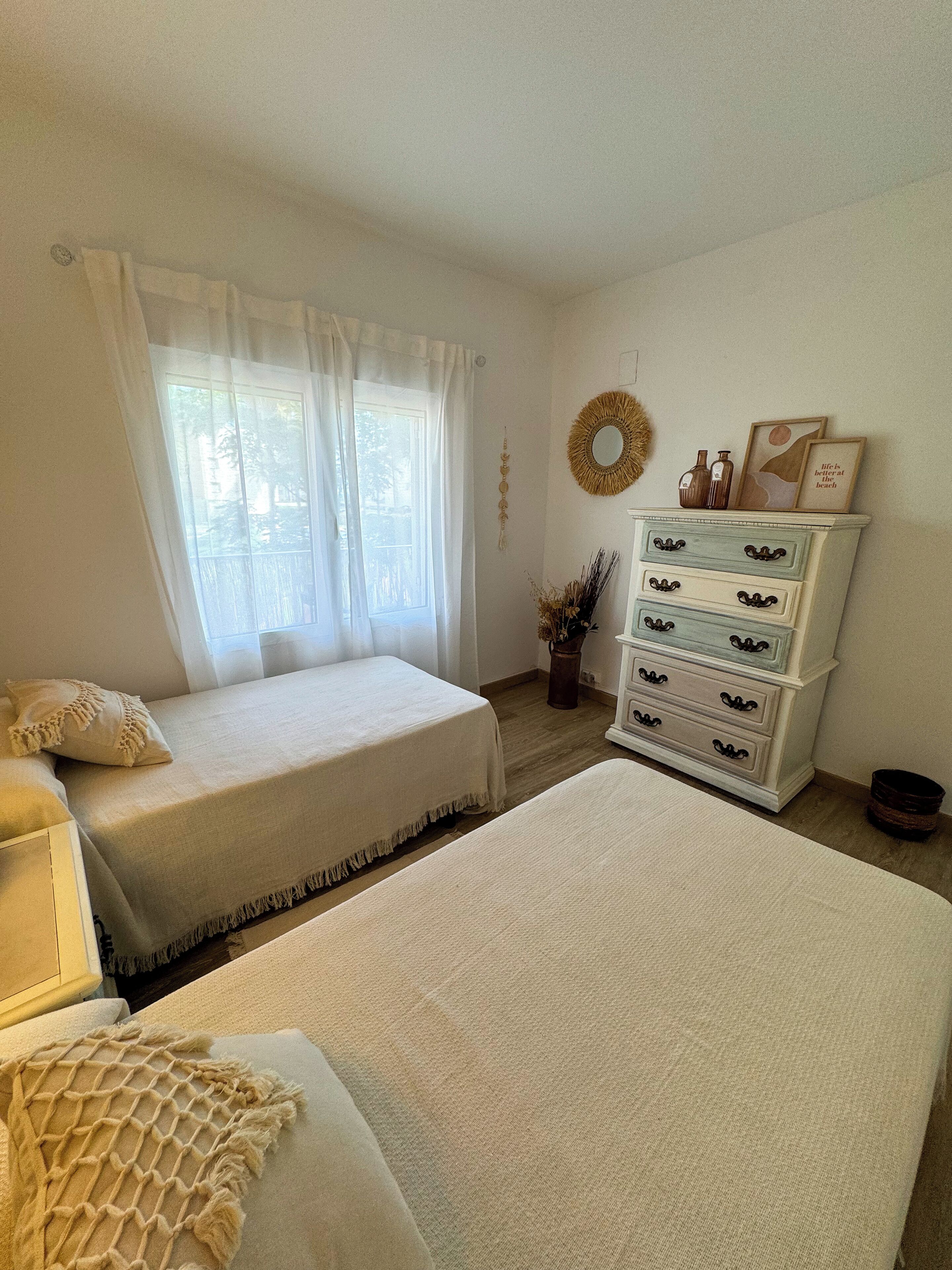 Un dormitorio con dos camas, un aparador, una ventana con cortinas y un adorno en la pared.