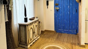 Um corredor com porta azul, piso de madeira, tapete decorativo, planta e um armário de estilo antigo.