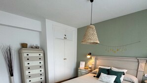 Quarto com cama, mesas de cabeceira, cômoda e luminária suspensa.