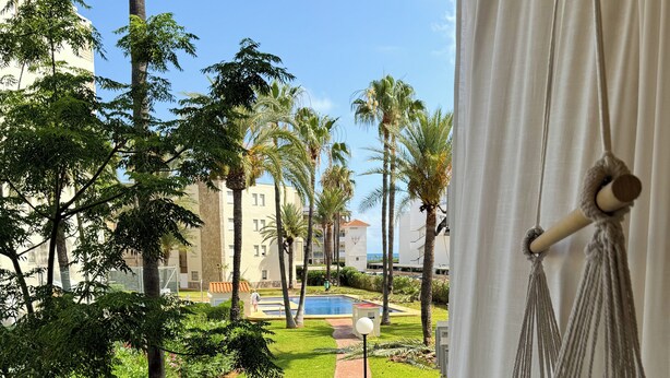 Uma varanda com vista para uma piscina, palmeiras e um edifício ao fundo.