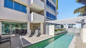 A modern building with a swimming pool, outdoor seating, and a covered area with a view of the pool.