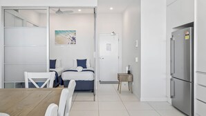 A modern hotel room with a bed, a small table, and a kitchenette.