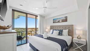 A modern hotel room with a large bed, a balcony with a view, a ceiling fan, and a painting on the wall.