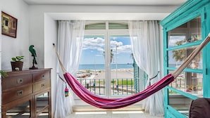Una habitación con vista a la playa, una hamaca, un armario de madera y un mueble de color aguamarina.