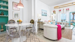 Una sala de estar moderna con un sofá blanco, una mesa redonda con sillas, y un comedor con una mesa y sillas blancas.