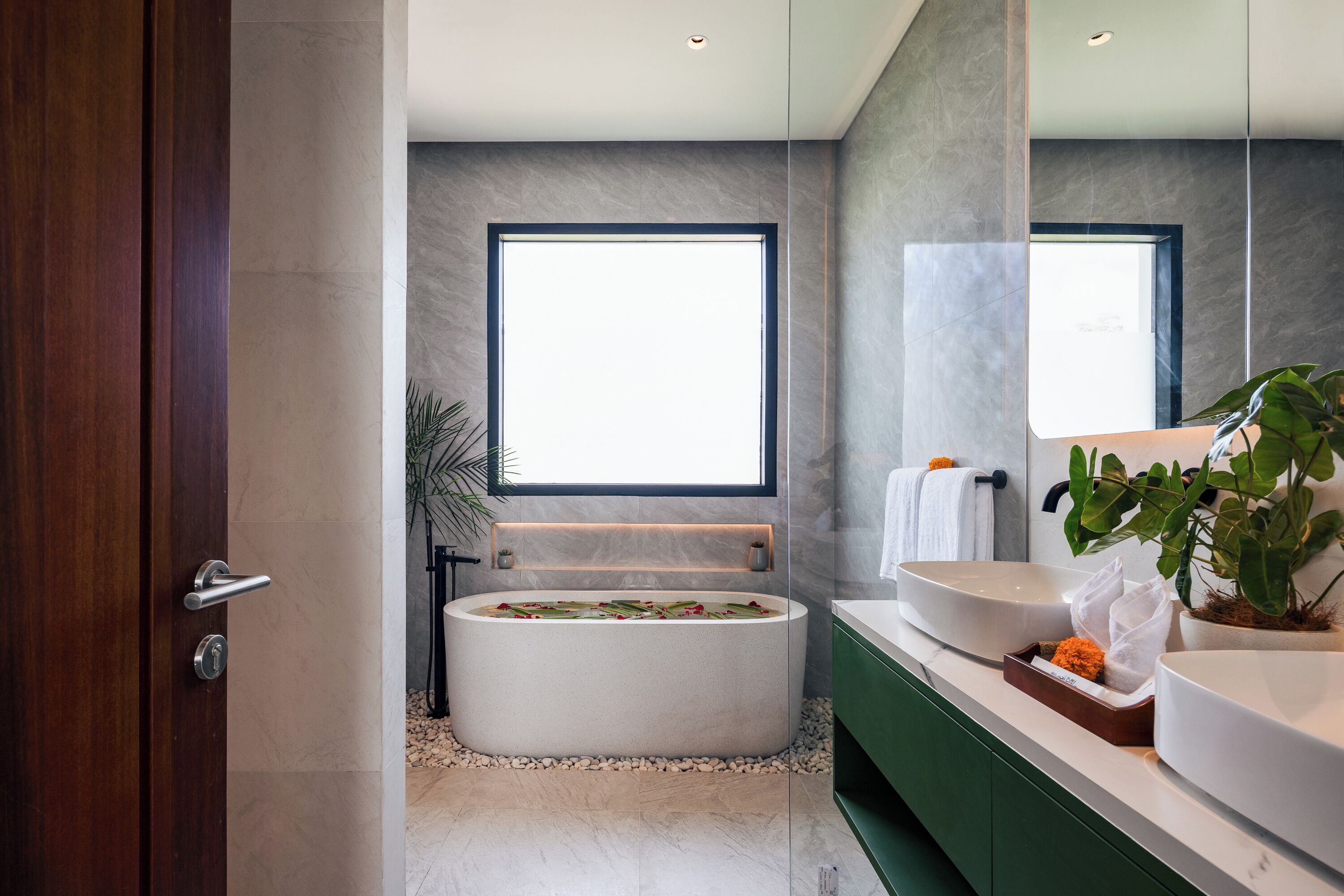 Un baño moderno con una bañera independiente, un espejo grande y un mueble de tocador verde.