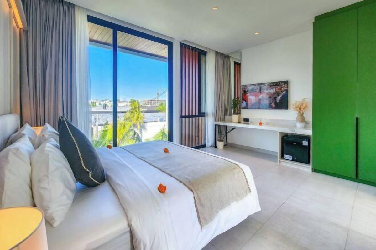 A modern hotel room with a large bed, a desk, and a green wardrobe.