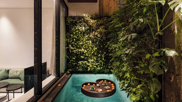 A modern indoor pool area with a floating platform, surrounded by lush greenery and a seating area with cushions. - Coco Jungle Canggu Villas by Nagisa Bali (Canggu)