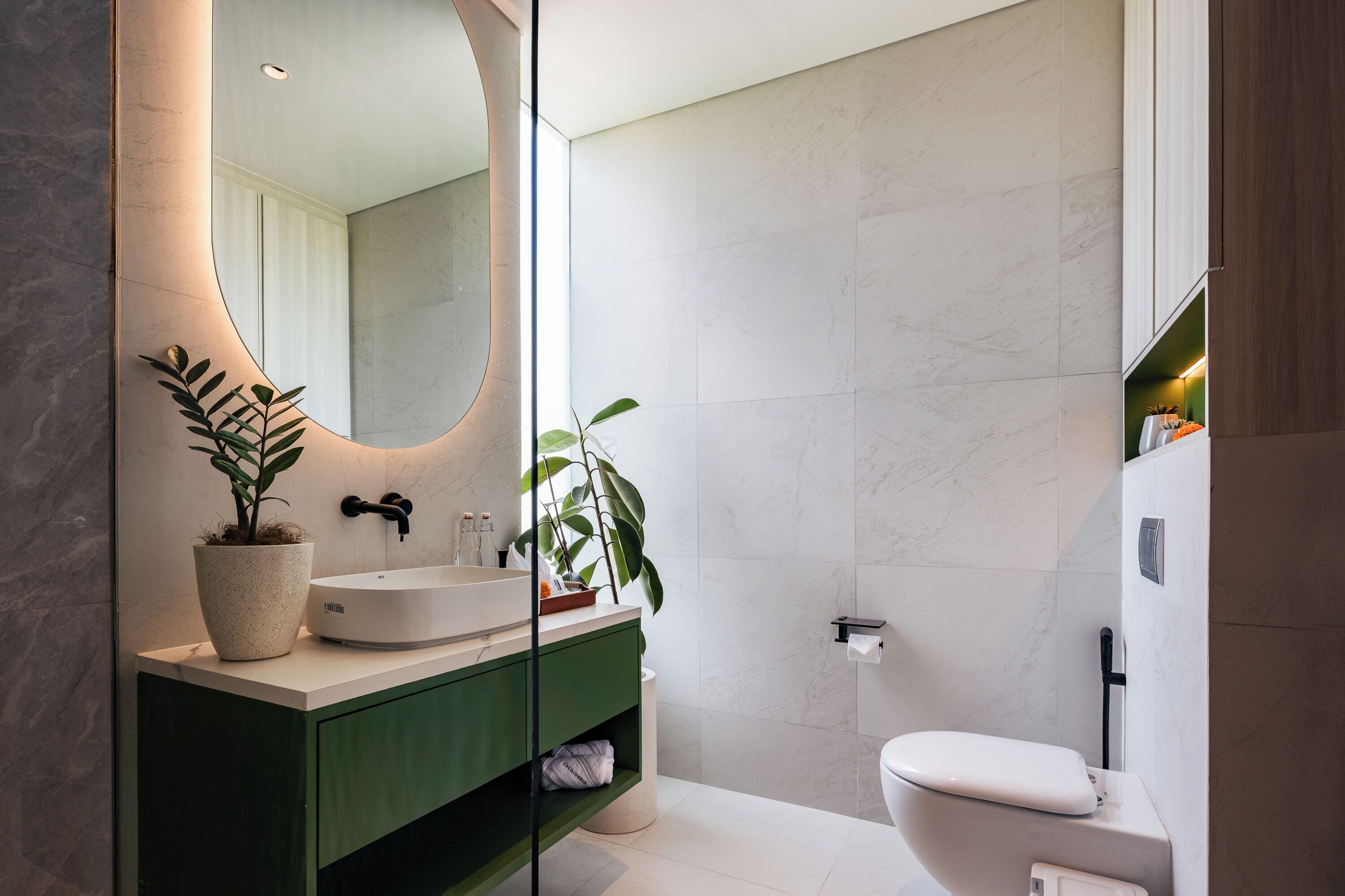 A modern bathroom with a white sink, green vanity, a large mirror, and a toilet.