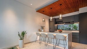 A modern kitchen with a wooden ceiling, bar stools, and a large window. - Coco Jungle Canggu Villas by Nagisa Bali (Canggu)