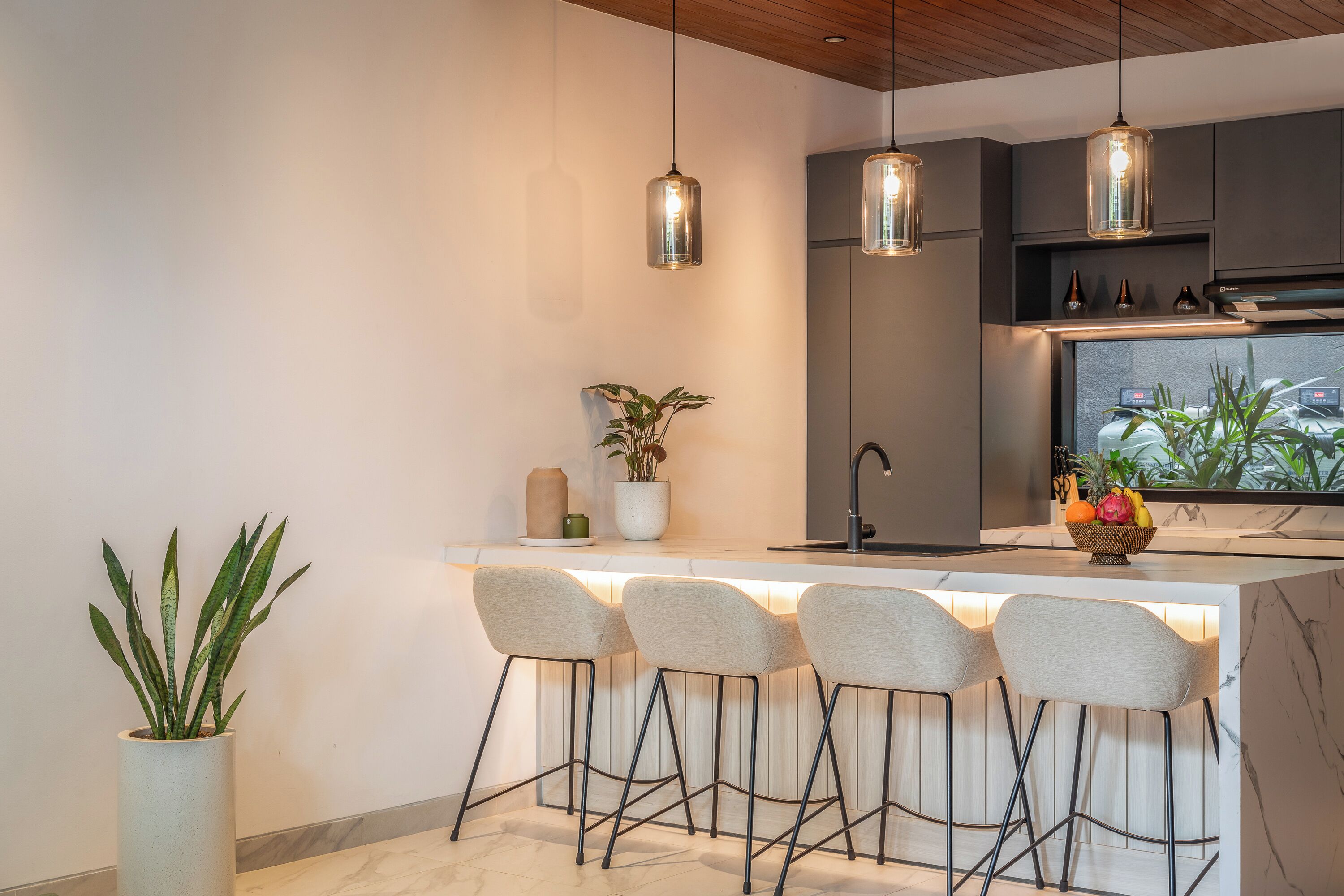 A modern kitchen with a central island, bar stools, pendant lighting, and a potted plant.